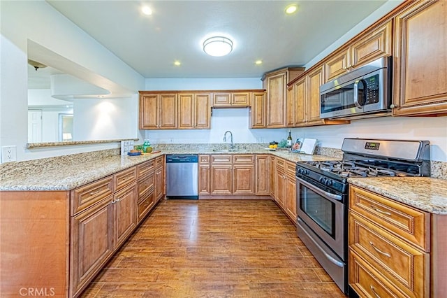 kitchen featuring light stone countertops, wood-type flooring, stainless steel appliances, sink, and kitchen peninsula