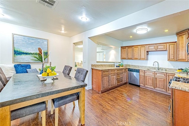 kitchen with light stone countertops, appliances with stainless steel finishes, wood-type flooring, and sink