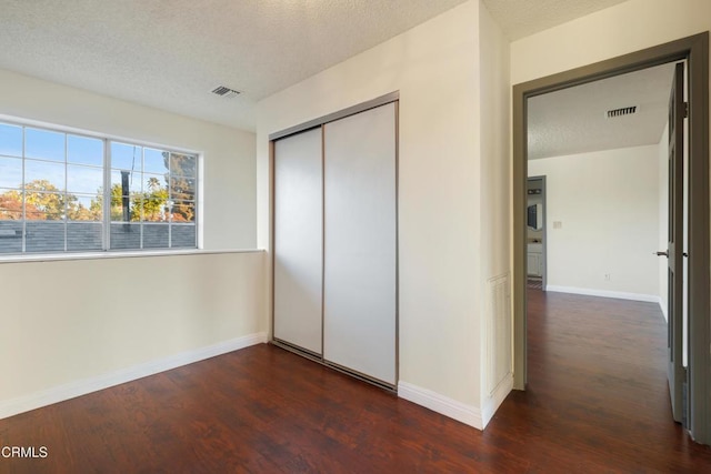 unfurnished bedroom with a textured ceiling, a closet, and dark hardwood / wood-style floors