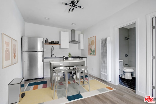 kitchen with tasteful backsplash, sink, stainless steel refrigerator, light wood-type flooring, and wall chimney exhaust hood