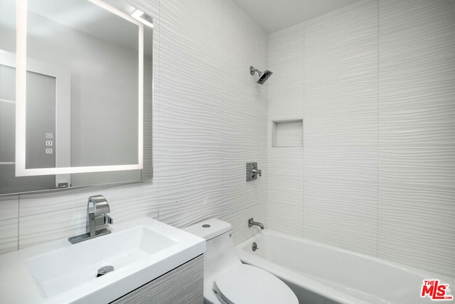 full bathroom with toilet, tiled shower / bath, backsplash, tile walls, and vanity