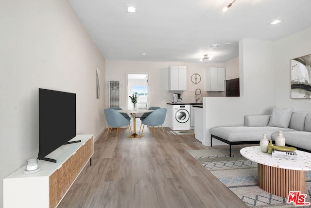 living room featuring light wood-type flooring, sink, and washer / dryer