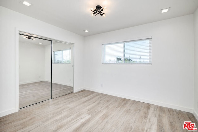 unfurnished bedroom featuring a closet, light hardwood / wood-style flooring, and multiple windows