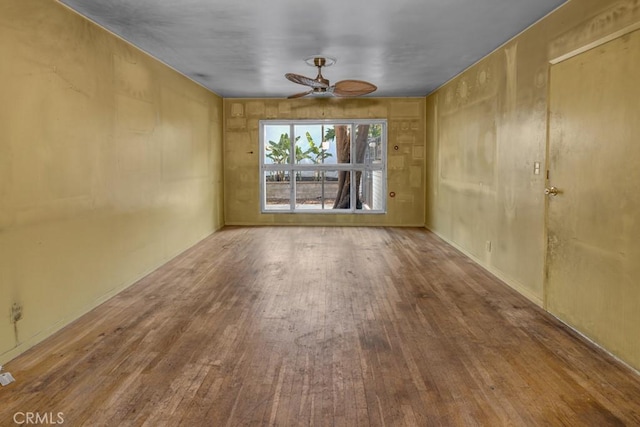 empty room featuring ceiling fan, wood walls, and hardwood / wood-style floors