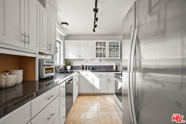 kitchen with stainless steel appliances, light tile patterned flooring, track lighting, white cabinets, and sink