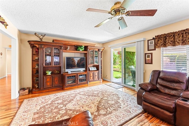 living room featuring ceiling fan, a textured ceiling, and light hardwood / wood-style flooring