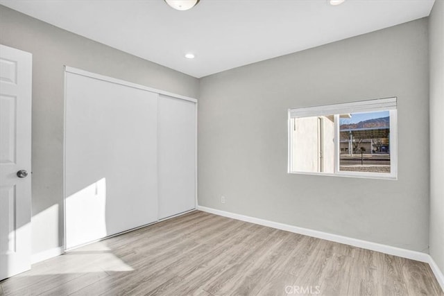 unfurnished bedroom with a closet, baseboards, wood finished floors, and recessed lighting