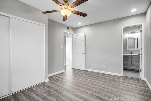 unfurnished bedroom featuring ensuite bathroom, hardwood / wood-style floors, a closet, and ceiling fan