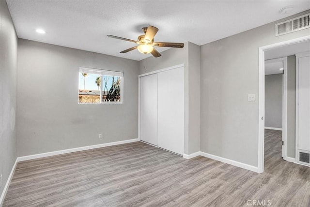 unfurnished bedroom with a textured ceiling, wood finished floors, visible vents, baseboards, and a closet