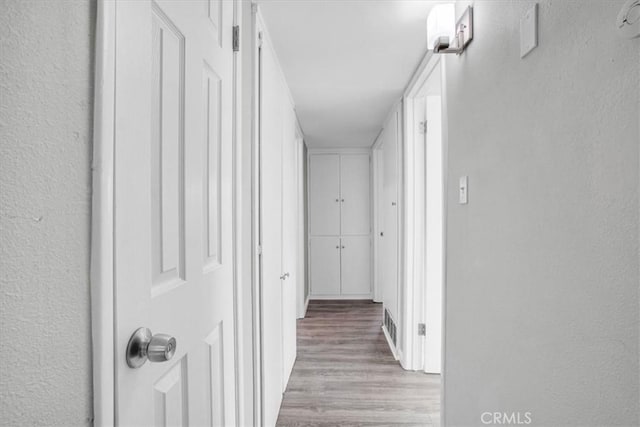 hall with a textured wall, wood finished floors, and visible vents