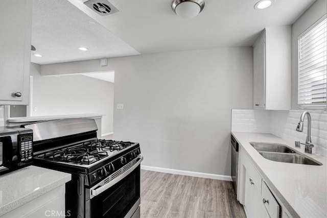 kitchen featuring stainless steel appliances, a sink, white cabinets, decorative backsplash, and light wood finished floors