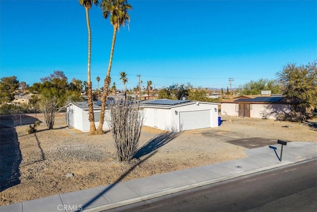 exterior space featuring concrete driveway, fence, and roof mounted solar panels