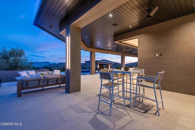 patio terrace at dusk featuring ceiling fan, an outdoor living space, and a mountain view