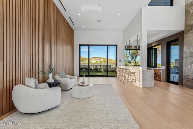 living room featuring light hardwood / wood-style flooring, wood walls, and a towering ceiling