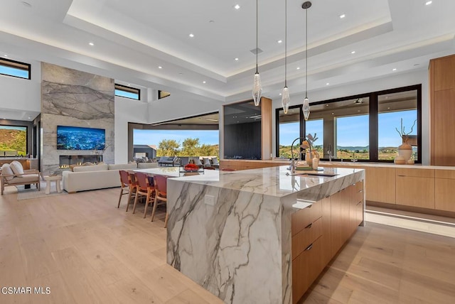 kitchen featuring a raised ceiling, a spacious island, decorative light fixtures, a fireplace, and light stone countertops