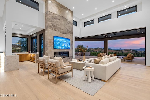 living room with a high ceiling, a stone fireplace, and light wood-type flooring