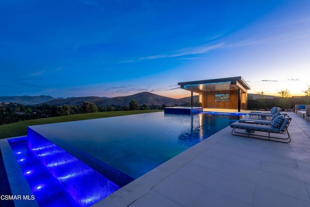 pool at dusk with a jacuzzi, a patio area, and a mountain view