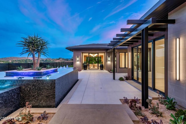 patio terrace at dusk featuring a mountain view and a pool with hot tub