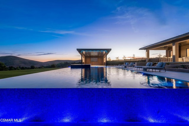 pool at dusk featuring a mountain view and a patio