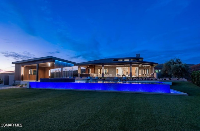 back house at dusk with a patio area and a yard