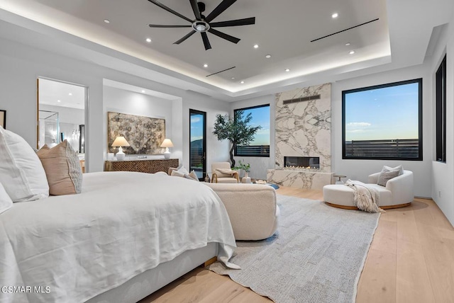 bedroom featuring ceiling fan, light hardwood / wood-style floors, a tray ceiling, and a fireplace