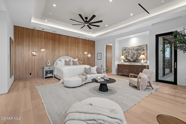 bedroom with access to outside, wooden walls, a tray ceiling, and light hardwood / wood-style flooring