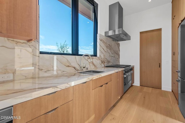 kitchen with stainless steel range, tasteful backsplash, wall chimney range hood, light stone counters, and sink