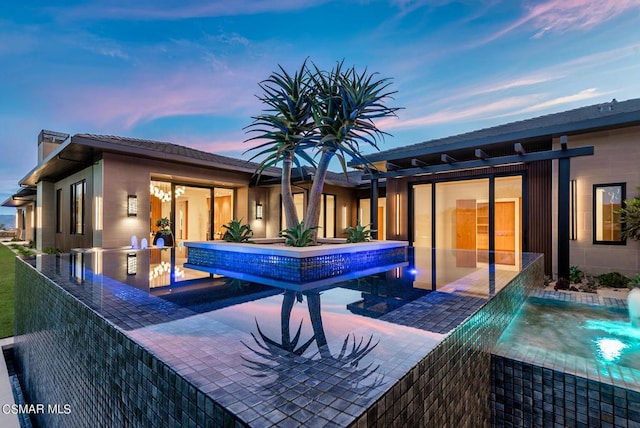 pool at dusk with pool water feature, an outdoor kitchen, and a patio