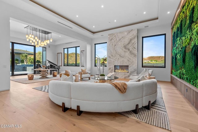 living room featuring a premium fireplace, light hardwood / wood-style floors, a raised ceiling, and a notable chandelier