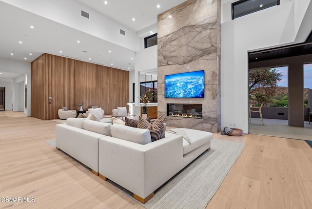 living room featuring a high ceiling, light wood-type flooring, wood walls, and a stone fireplace