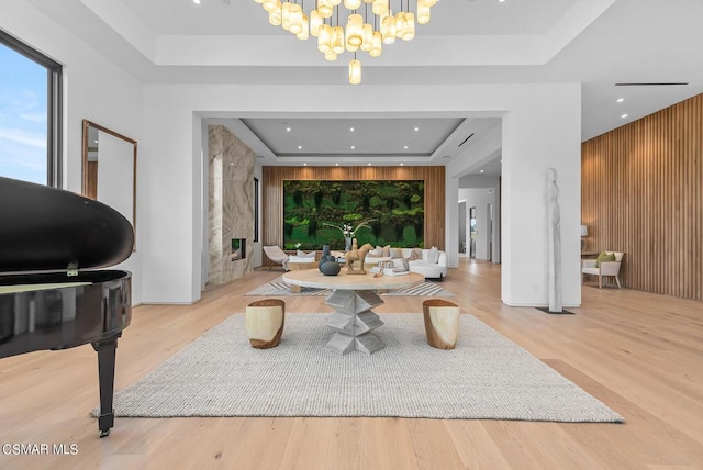 living room featuring an inviting chandelier, light hardwood / wood-style floors, wood walls, and a tray ceiling