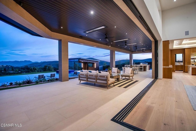 patio terrace at dusk featuring a mountain view, ceiling fan, and outdoor lounge area