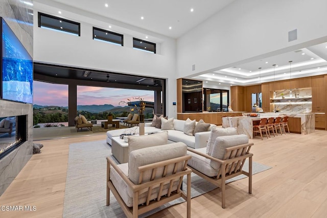 living room featuring a fireplace, a tray ceiling, a towering ceiling, and light hardwood / wood-style flooring