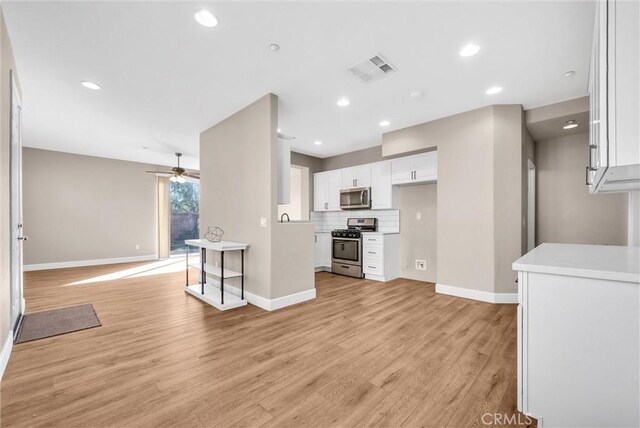 kitchen with ceiling fan, backsplash, light wood-type flooring, appliances with stainless steel finishes, and white cabinets