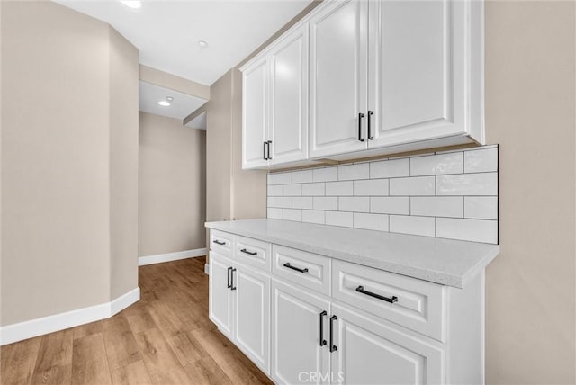 kitchen with white cabinetry, decorative backsplash, light hardwood / wood-style flooring, and light stone counters