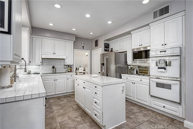 kitchen featuring stainless steel appliances, sink, a center island, white cabinetry, and decorative backsplash