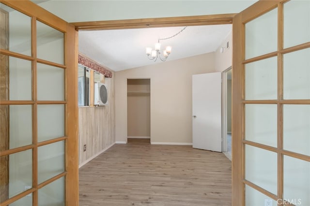 corridor featuring light wood-type flooring, a notable chandelier, and vaulted ceiling