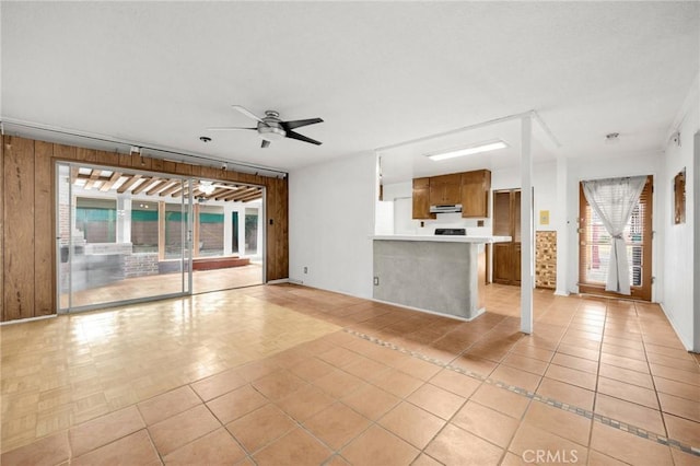 unfurnished living room with ceiling fan, light tile patterned floors, and wooden walls