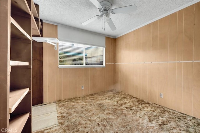 carpeted spare room with a textured ceiling, ceiling fan, crown molding, and wooden walls