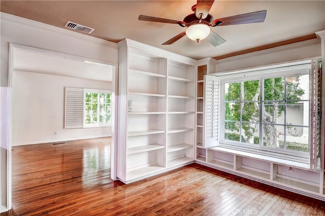 spare room with wood-type flooring, a healthy amount of sunlight, ceiling fan, and built in shelves