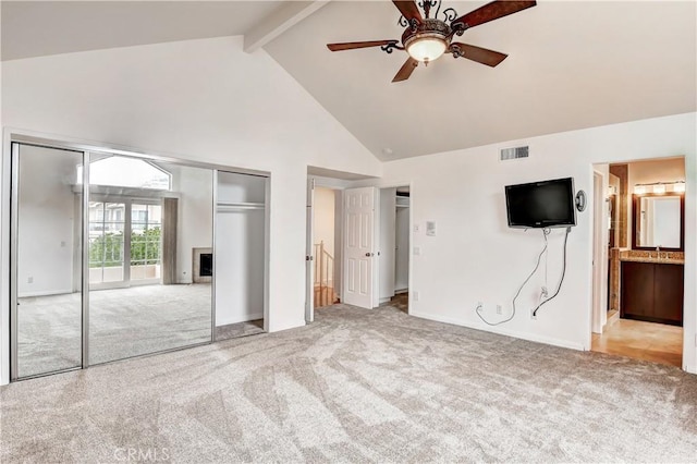 unfurnished bedroom featuring ensuite bath, high vaulted ceiling, light colored carpet, beamed ceiling, and ceiling fan