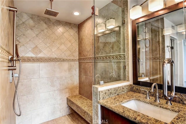 bathroom with a tile shower, vanity, and tile walls