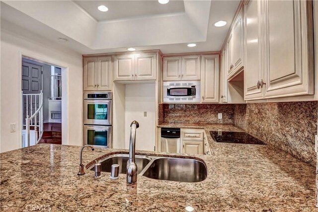 kitchen with stainless steel appliances, sink, light stone counters, and a tray ceiling