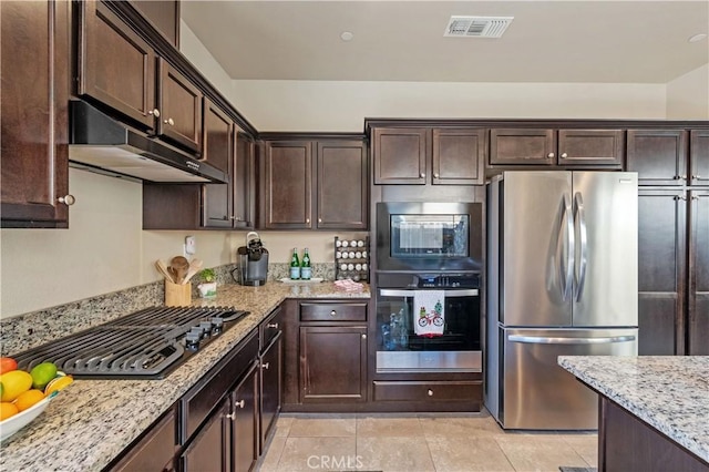 kitchen with light stone countertops, appliances with stainless steel finishes, dark brown cabinets, and light tile patterned flooring