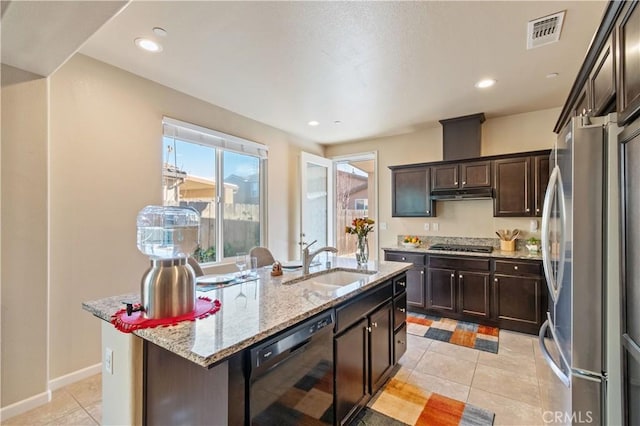 kitchen with light tile patterned floors, appliances with stainless steel finishes, a kitchen island with sink, light stone counters, and sink