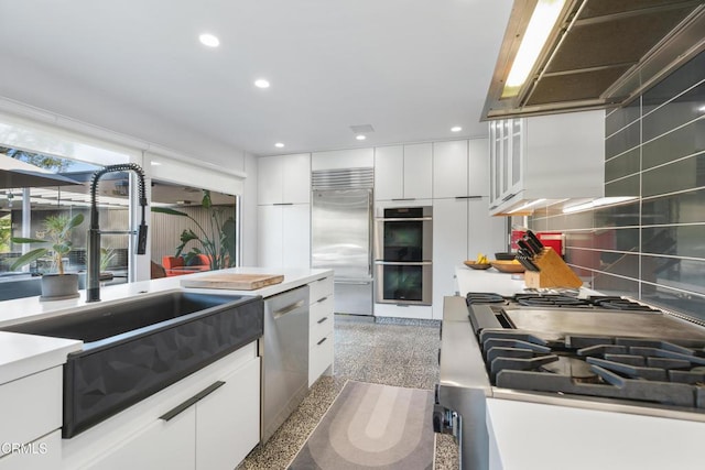 kitchen with custom exhaust hood, white cabinets, sink, and stainless steel appliances