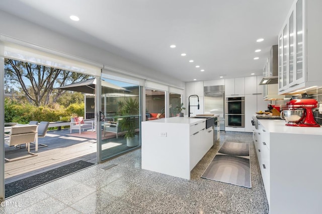 kitchen with white cabinetry, appliances with stainless steel finishes, a kitchen island with sink, wall chimney range hood, and sink