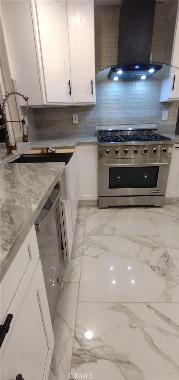 kitchen featuring high end range, wall chimney range hood, light stone counters, and white cabinets