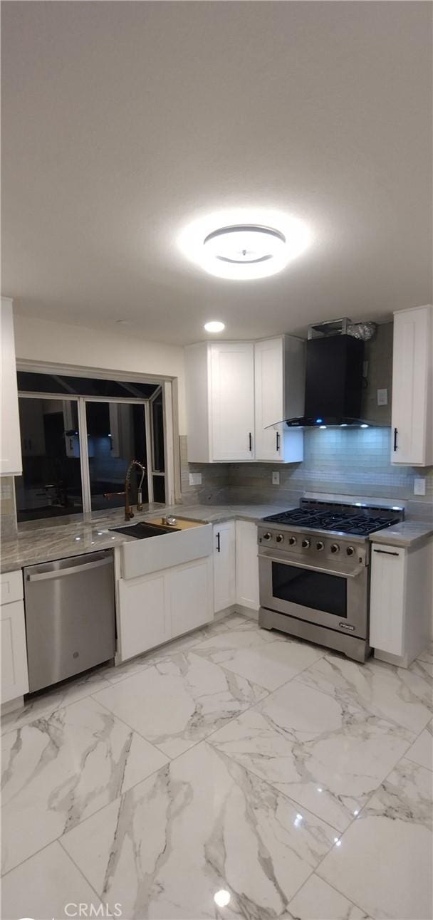 kitchen with wall chimney range hood, sink, backsplash, stainless steel appliances, and white cabinets