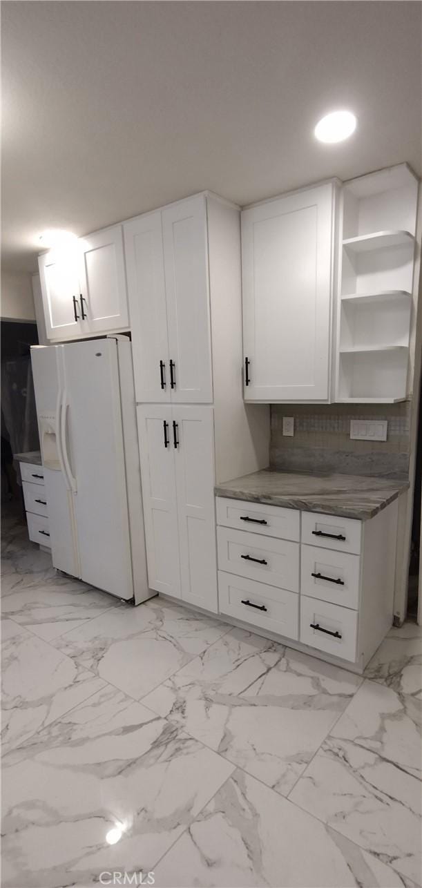 kitchen with tasteful backsplash, white fridge with ice dispenser, and white cabinets